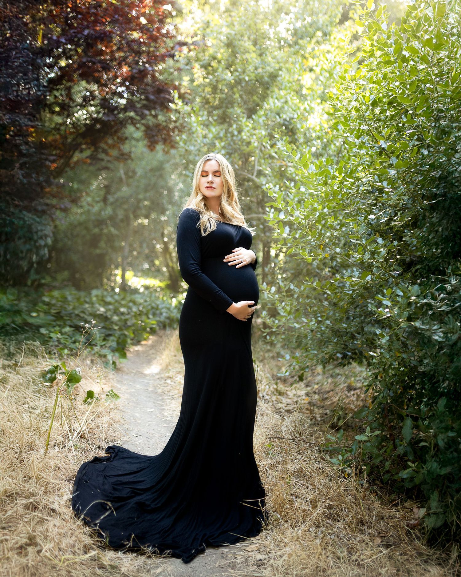 A figure in a flowing black dress sits gracefully among lush greenery in a dreamy outdoor setting.