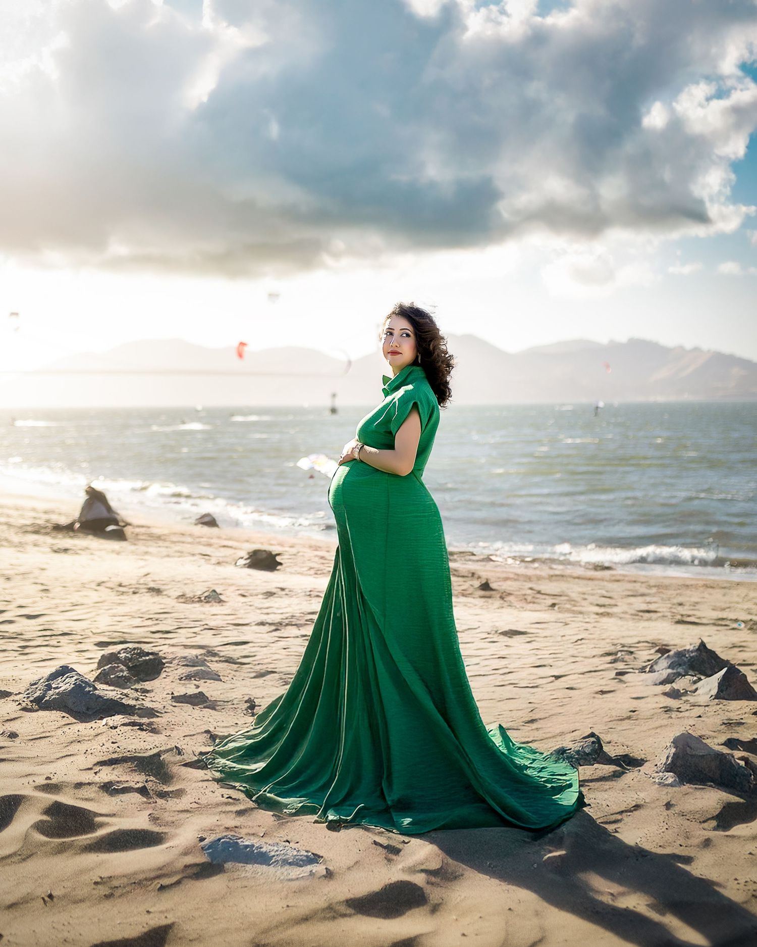 A flowing emerald green dress billows dramatically against the scenic backdrop of a misty beach at sunset.