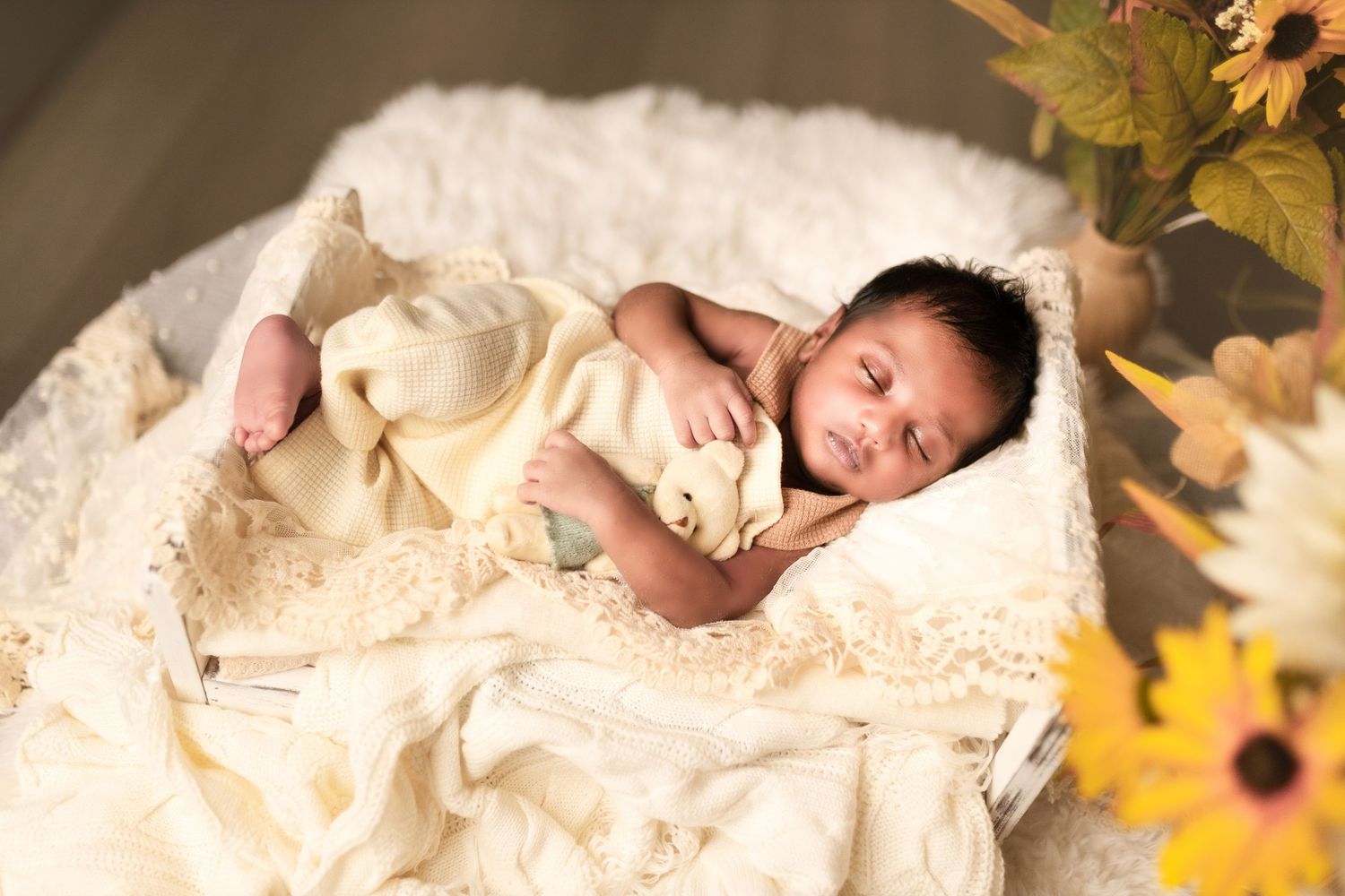 Newborn baby sleeping peacefully on white blankets surrounded by soft autumn leaves and natural light.