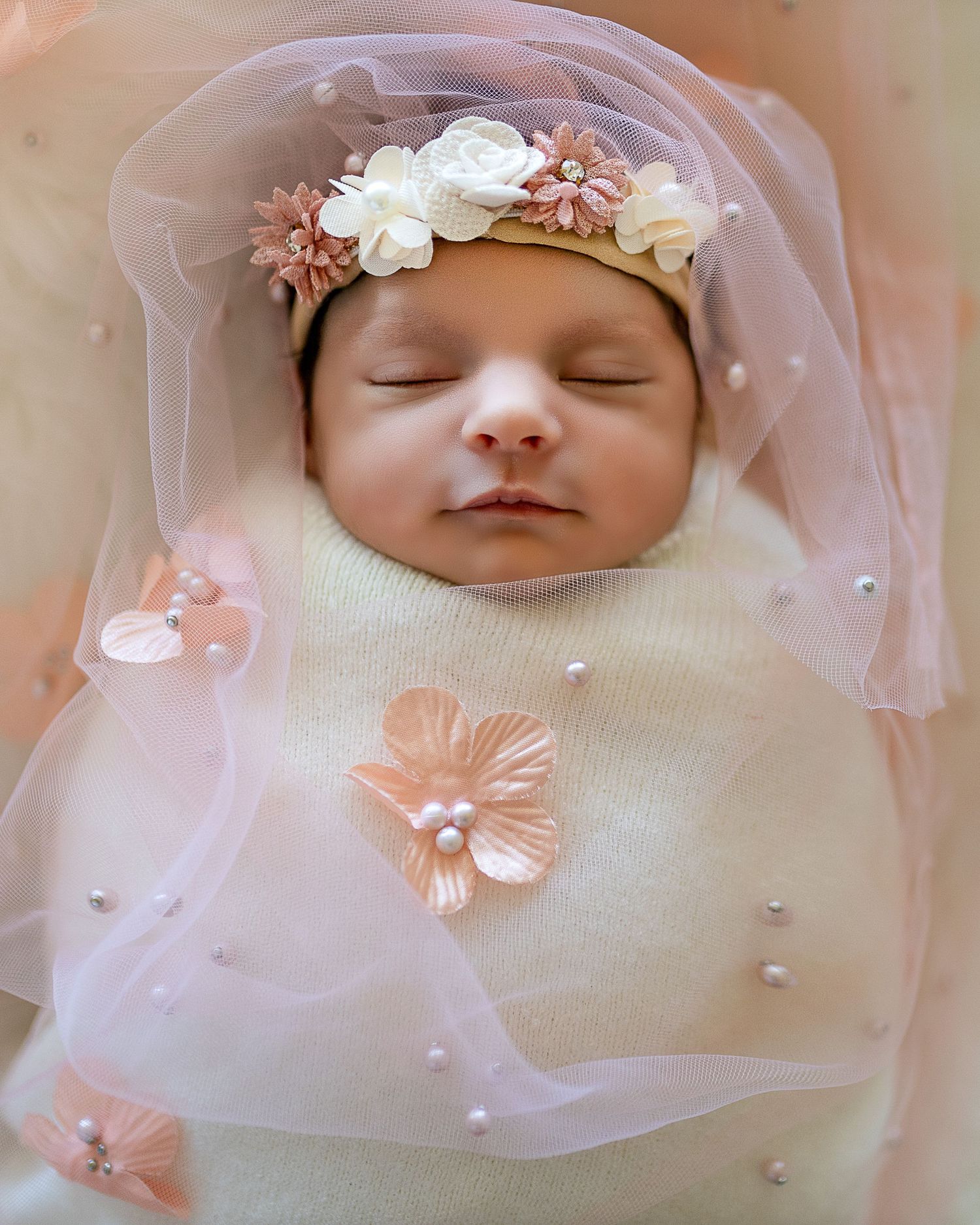 Sleeping newborn wearing delicate floral crown and pink tulle veil in dreamy portrait series.