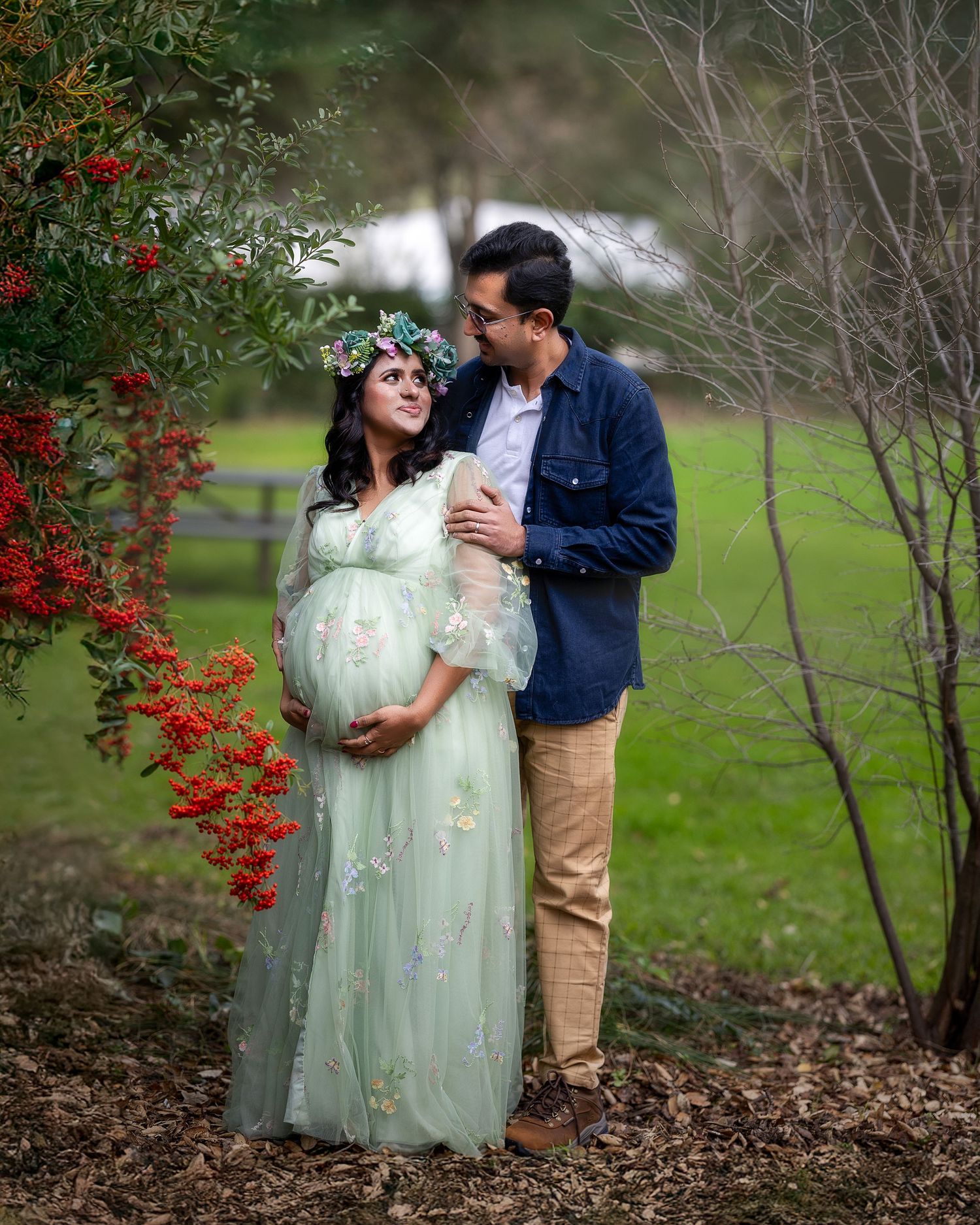 A romantic maternity photo in a garden setting with red berries and a flowing mint green dress.
