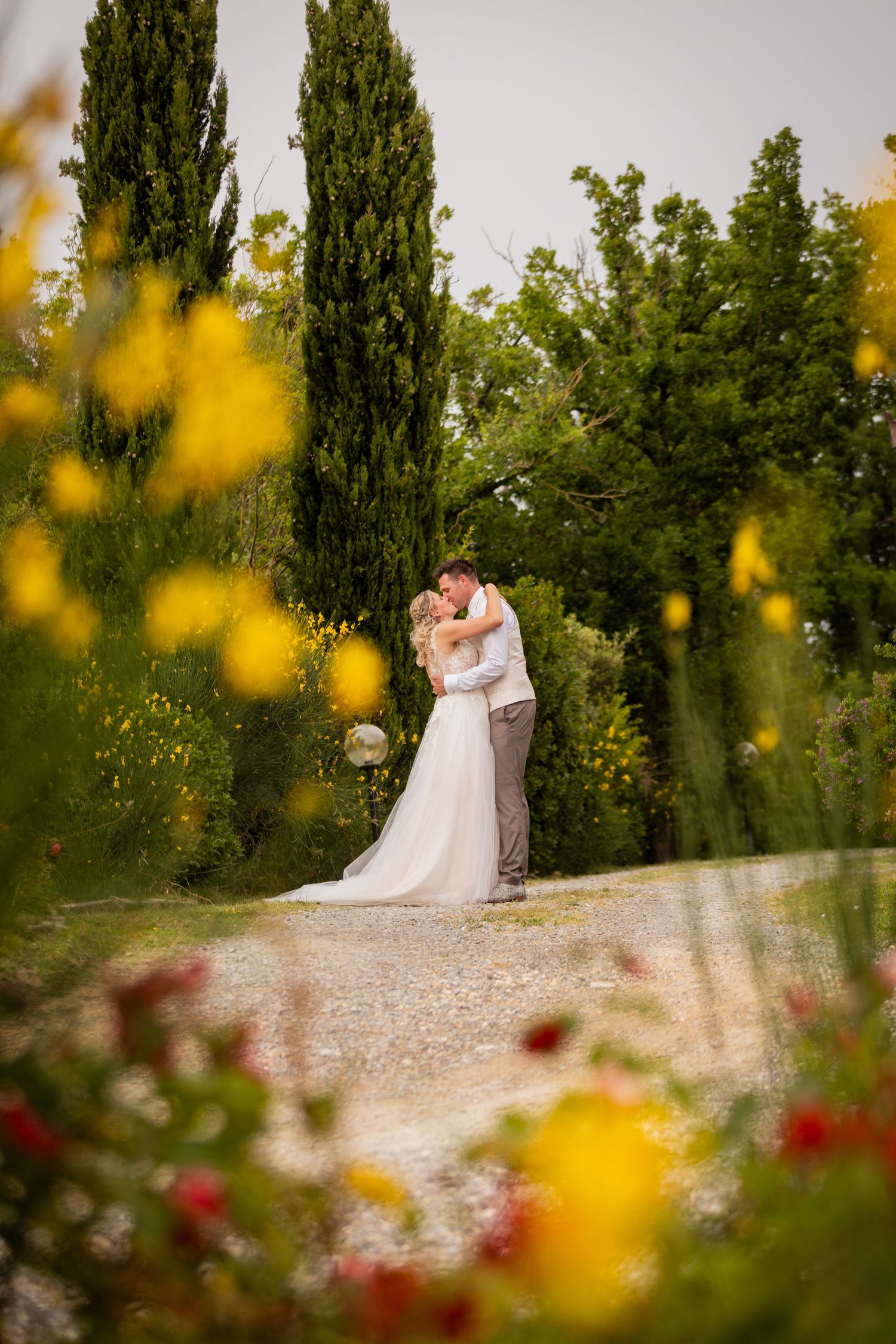 Newlyweds share an intimate moment in a garden setting with yellow and red flowers in the foreground.