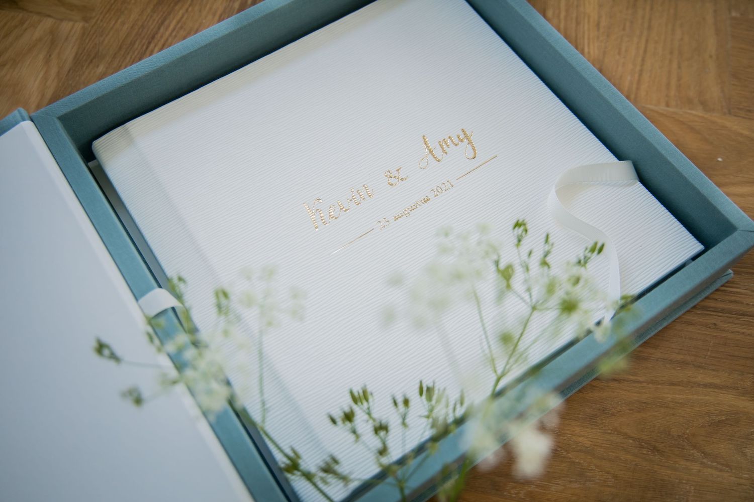 Delicate white flowers and foliage arranged in a light blue frame against a wooden surface.