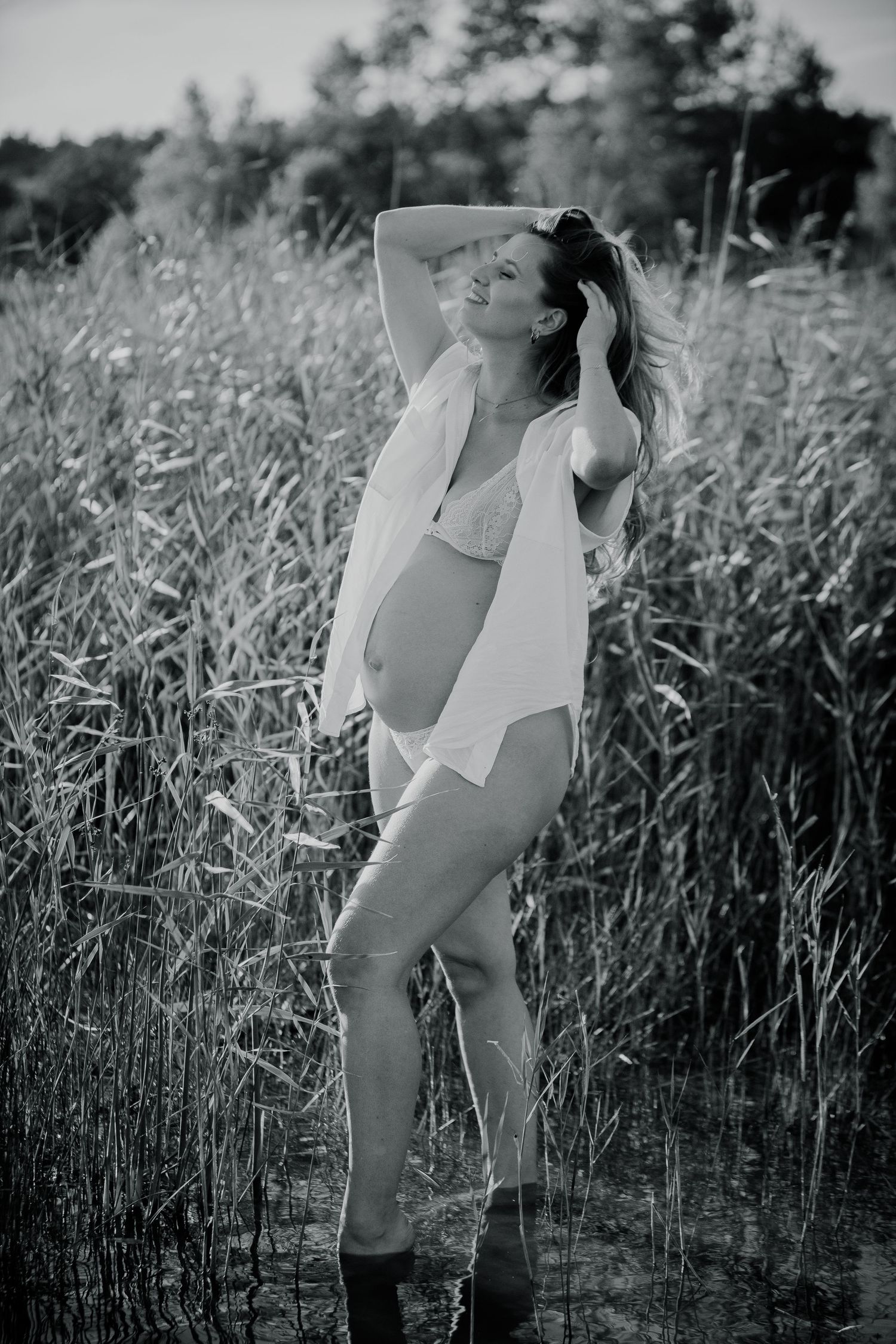 Black and white portrait of expectant mother in tall grass wearing light colored clothing.