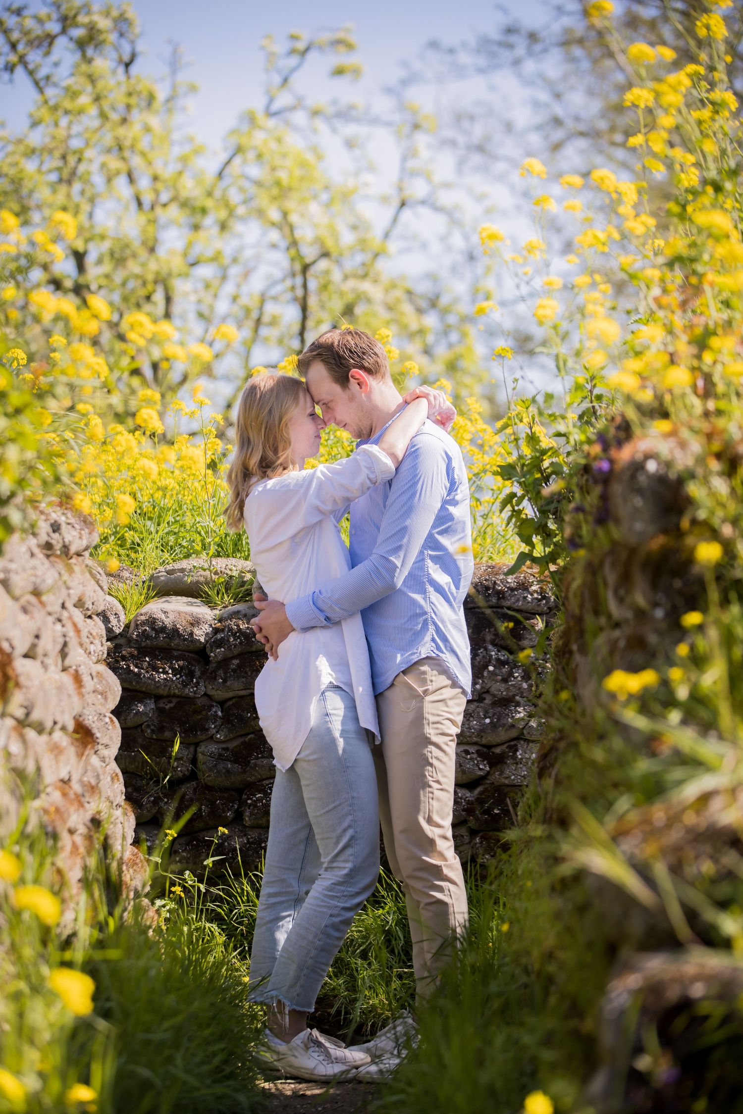 A tender embrace against a stone wall surrounded by vibrant yellow spring flowers.