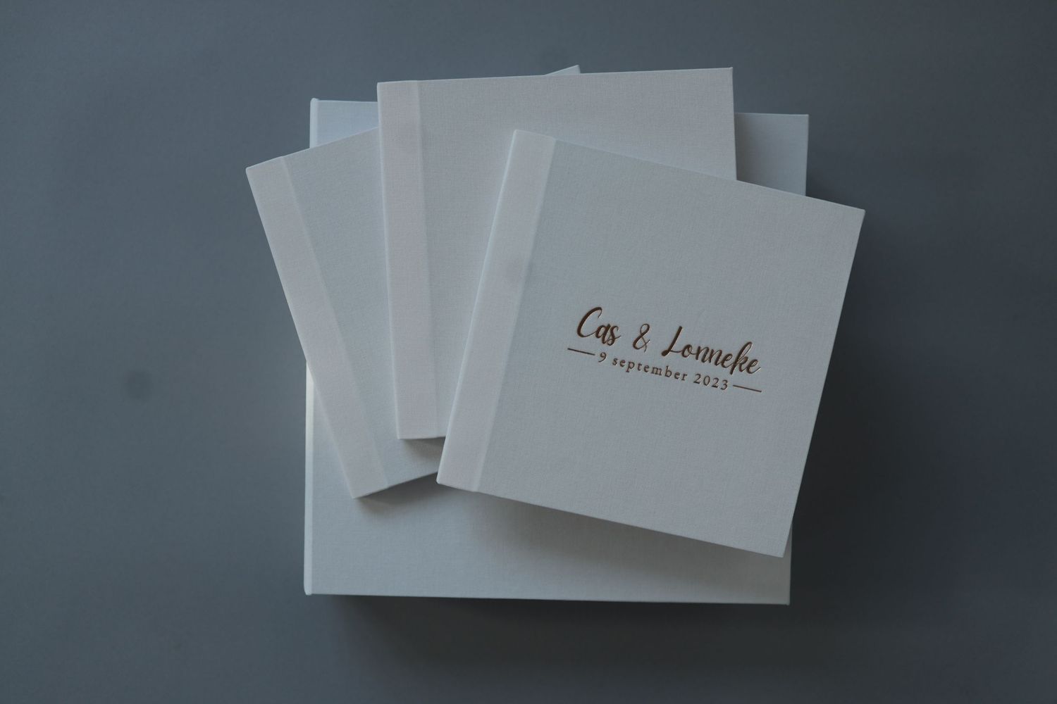 White wedding invitation cards with elegant brown text stacked on a gray surface.