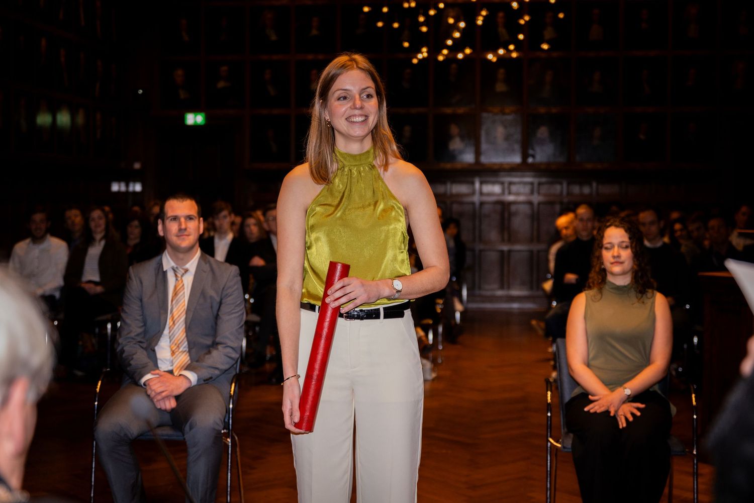 A person in a yellow top stands to give a speech at an evening event.