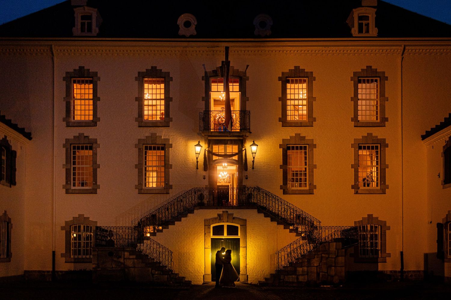 Elegant historic mansion illuminated at night with glowing windows and grand double staircase entrance.