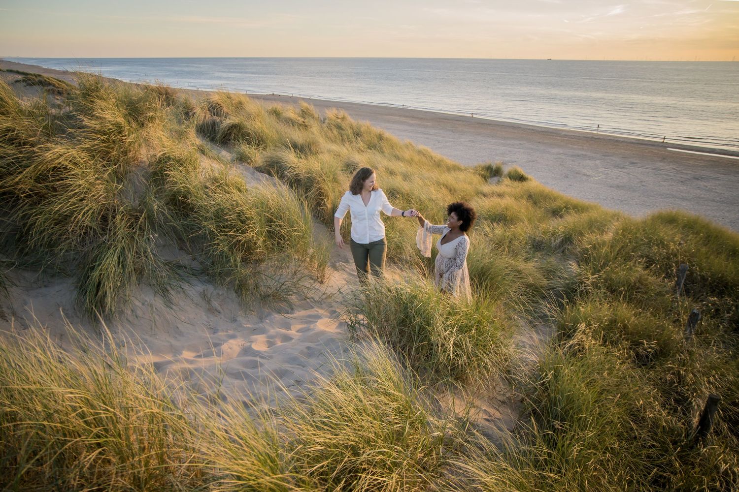 Family walking together on coastal sand dunes with ocean view at sunset.