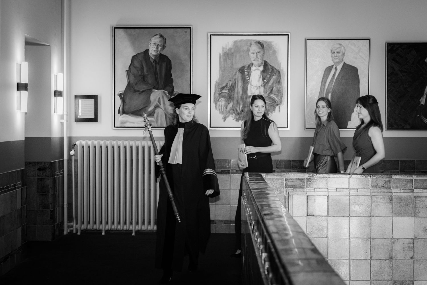 Black and white photo of people viewing portraits in an art gallery.