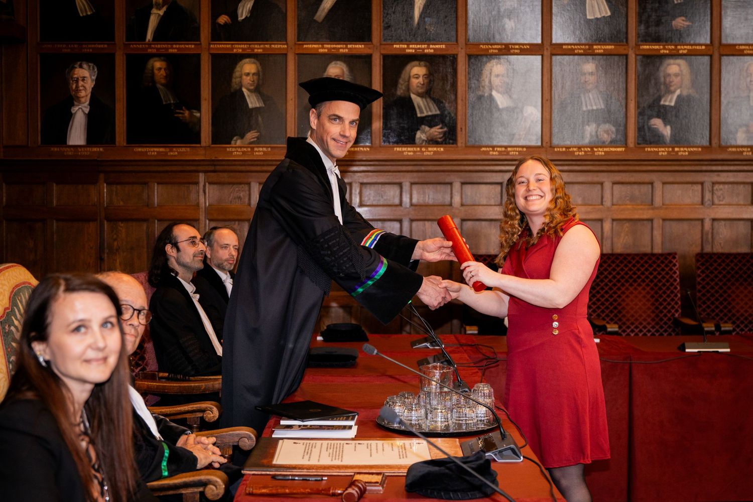 Elegantly dressed people celebrating in a wood-paneled formal room.