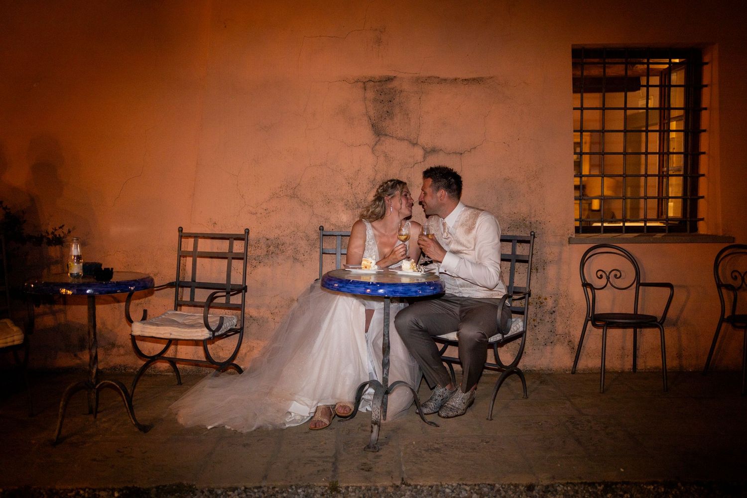 Bride and groom share an intimate moment while dining at a rustic outdoor reception table.