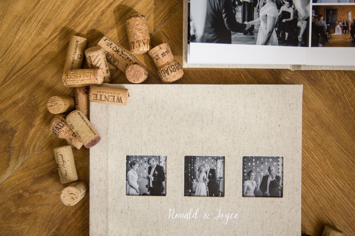 Wine corks are scattered around a wedding photo album with black and white photos on wooden surface.