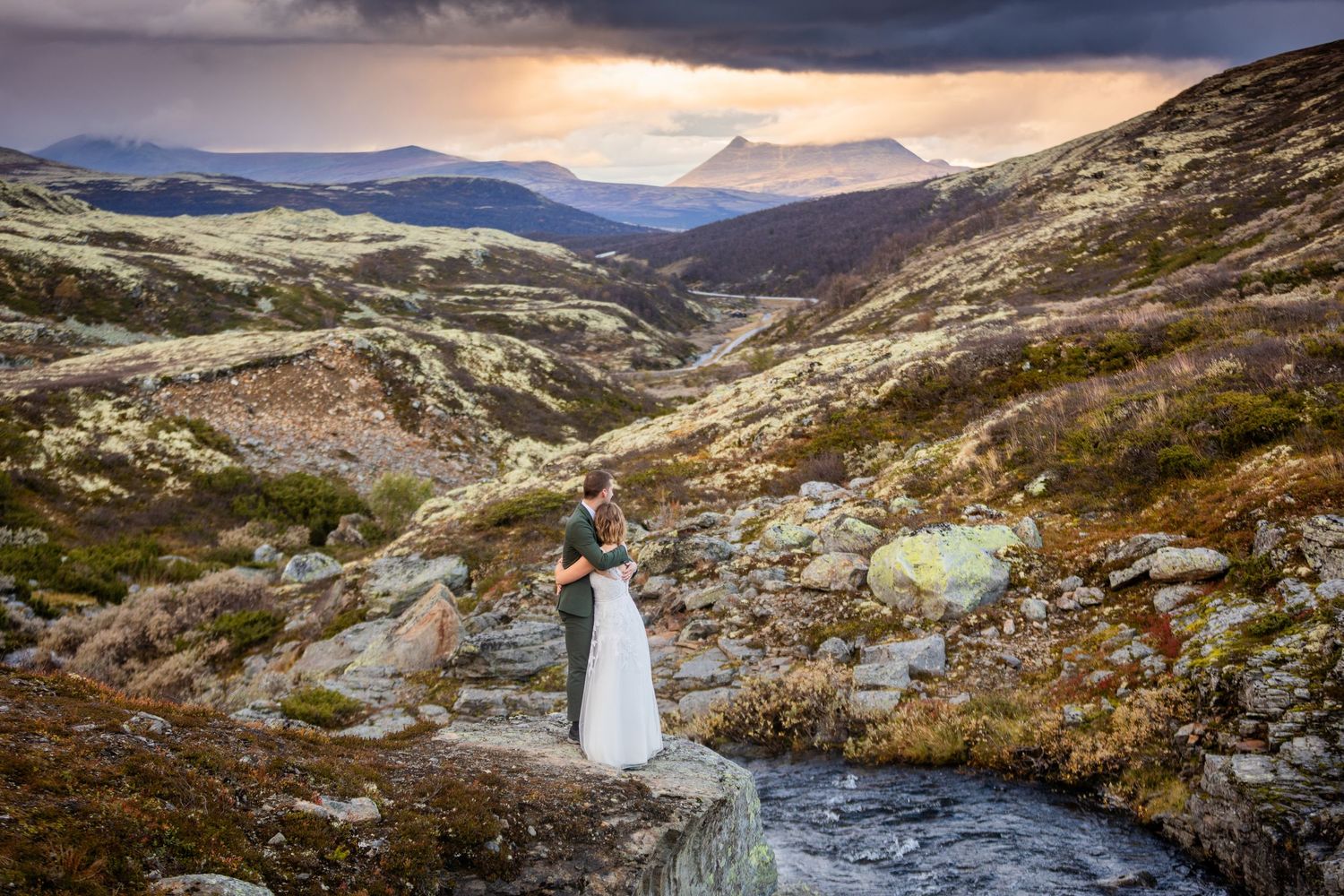 A sweeping mountain vista with dramatic clouds and winding stream through rocky terrain.