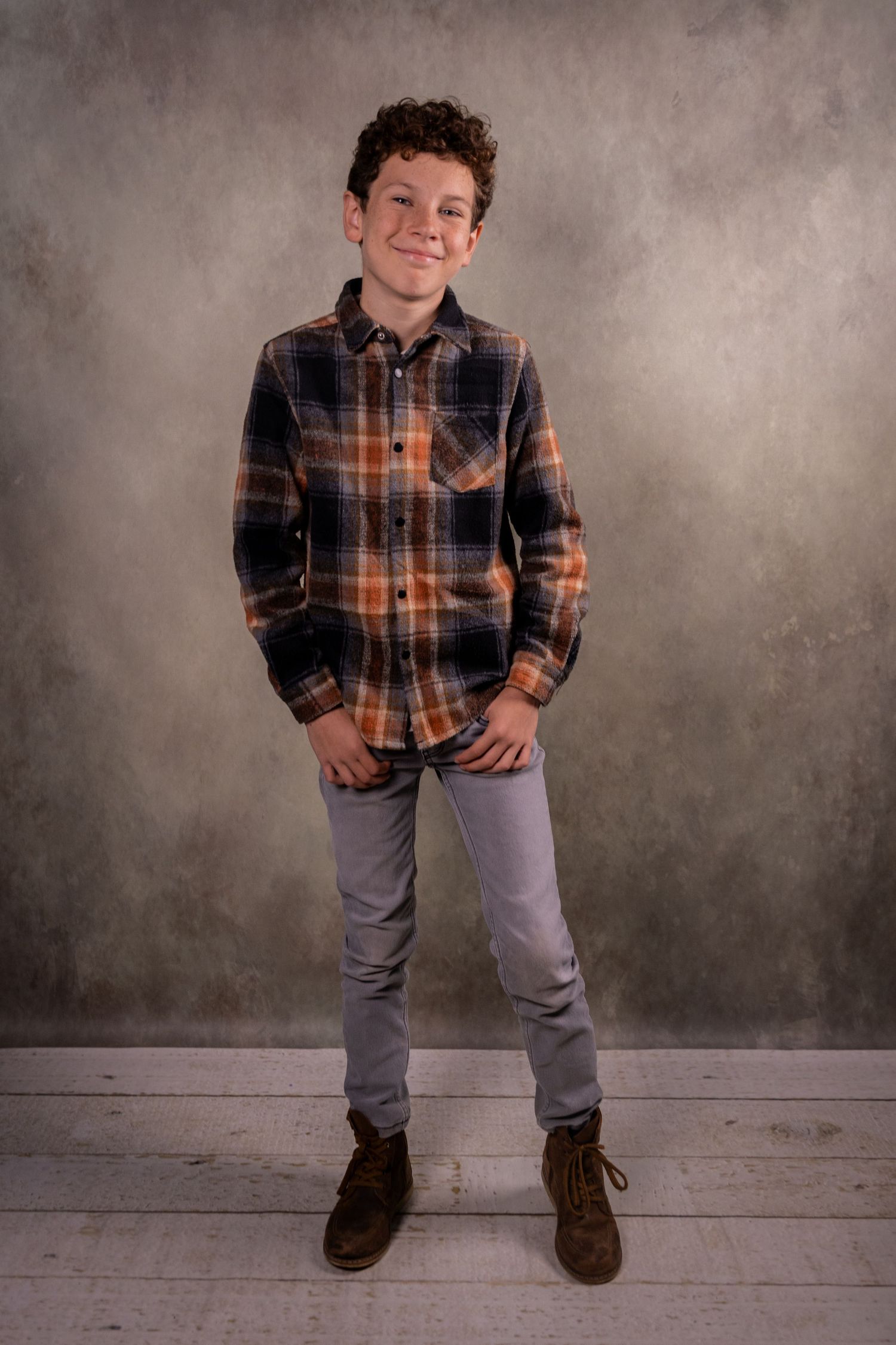 Full length studio portrait of a person in plaid shirt and jeans against a neutral backdrop.