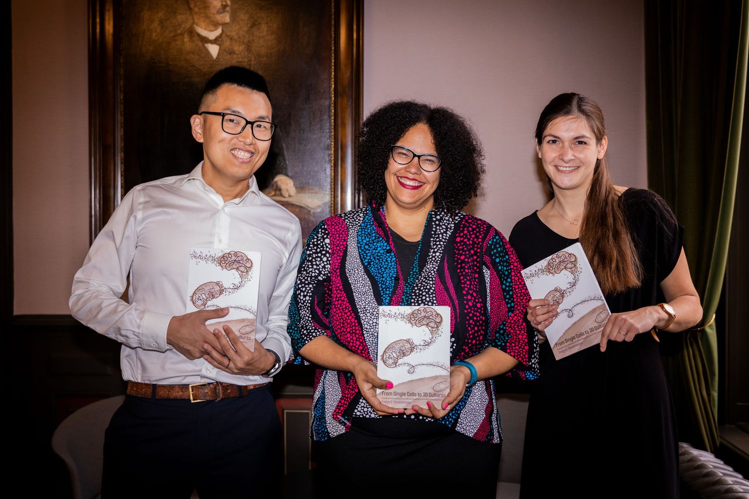 Three people pose together while holding books at a publishing event.