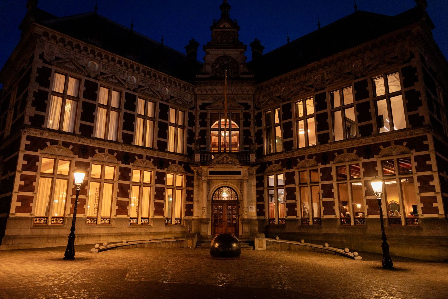 Historic university building illuminated at night with ornate gothic architecture and glowing windows.