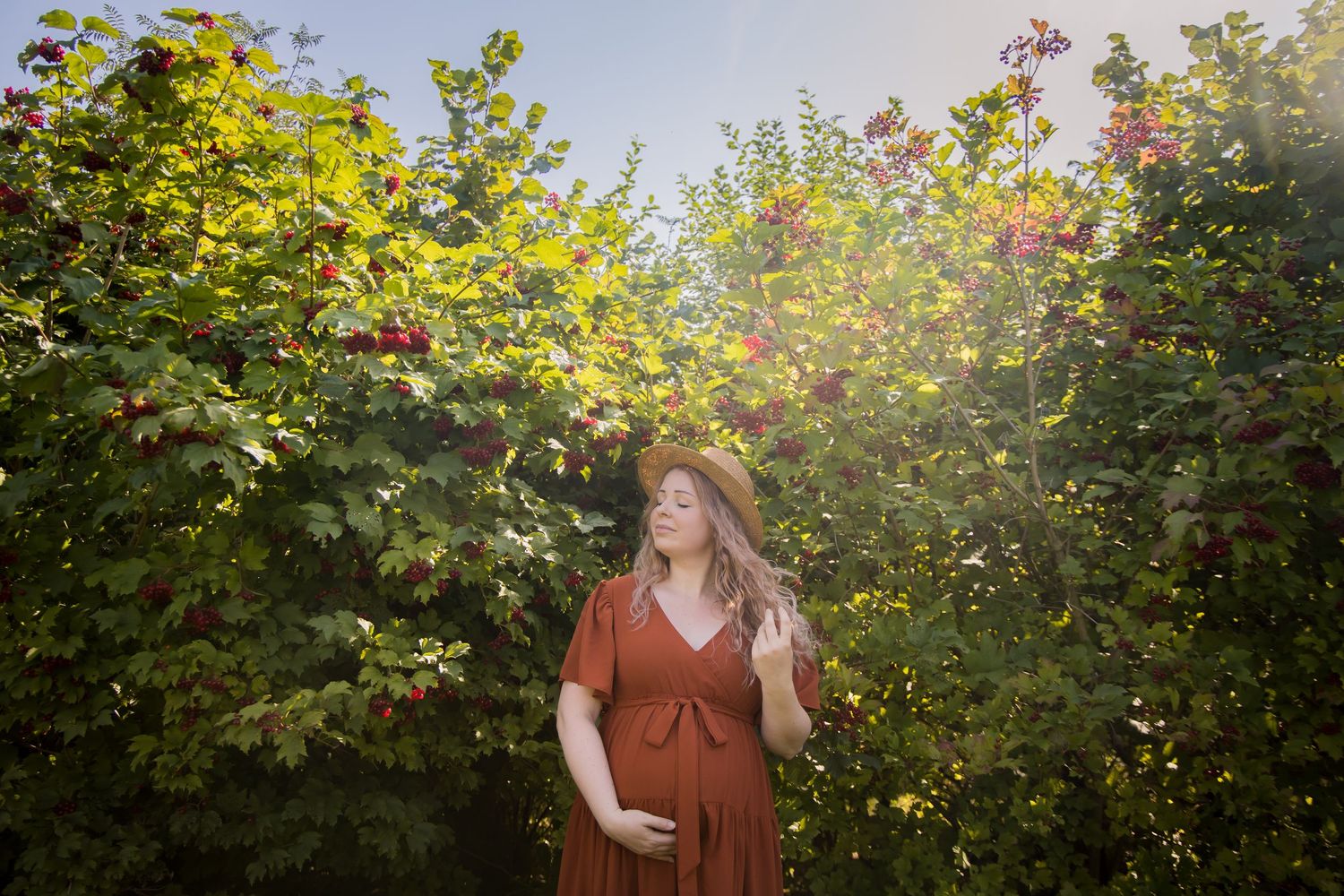 Woman in brown dress posing in garden with blooming flowers and sunlit foliage.