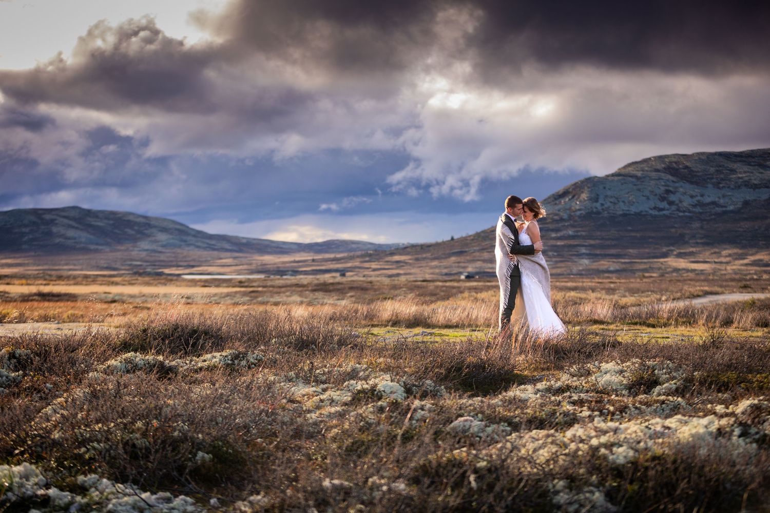 Newlywed couple posing in dramatic Scottish Highland landscape under cloudy skies.