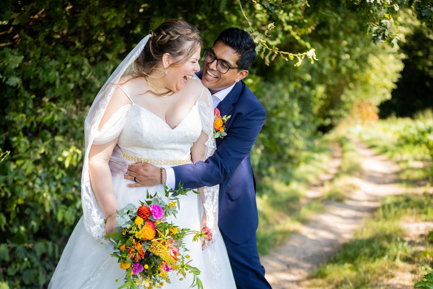 Joyful moment between couple on tree-lined path with colorful bouquet.