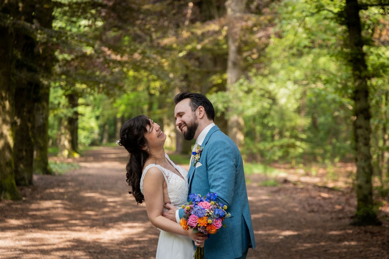 Romantic wedding portrait of couple sharing a joyful moment in a sunlit forest path.