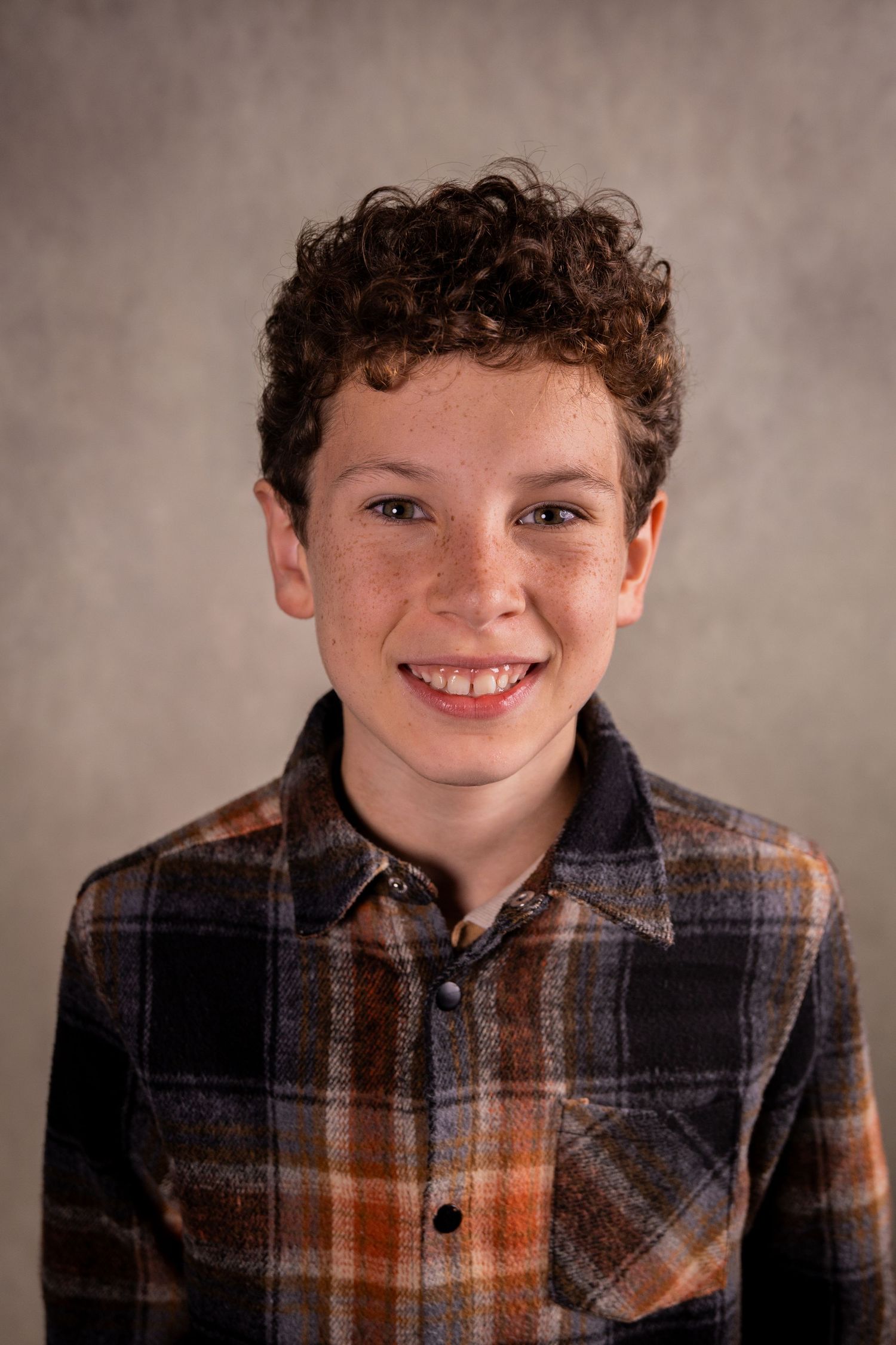 Studio headshot of a person wearing a plaid flannel shirt against a neutral background.