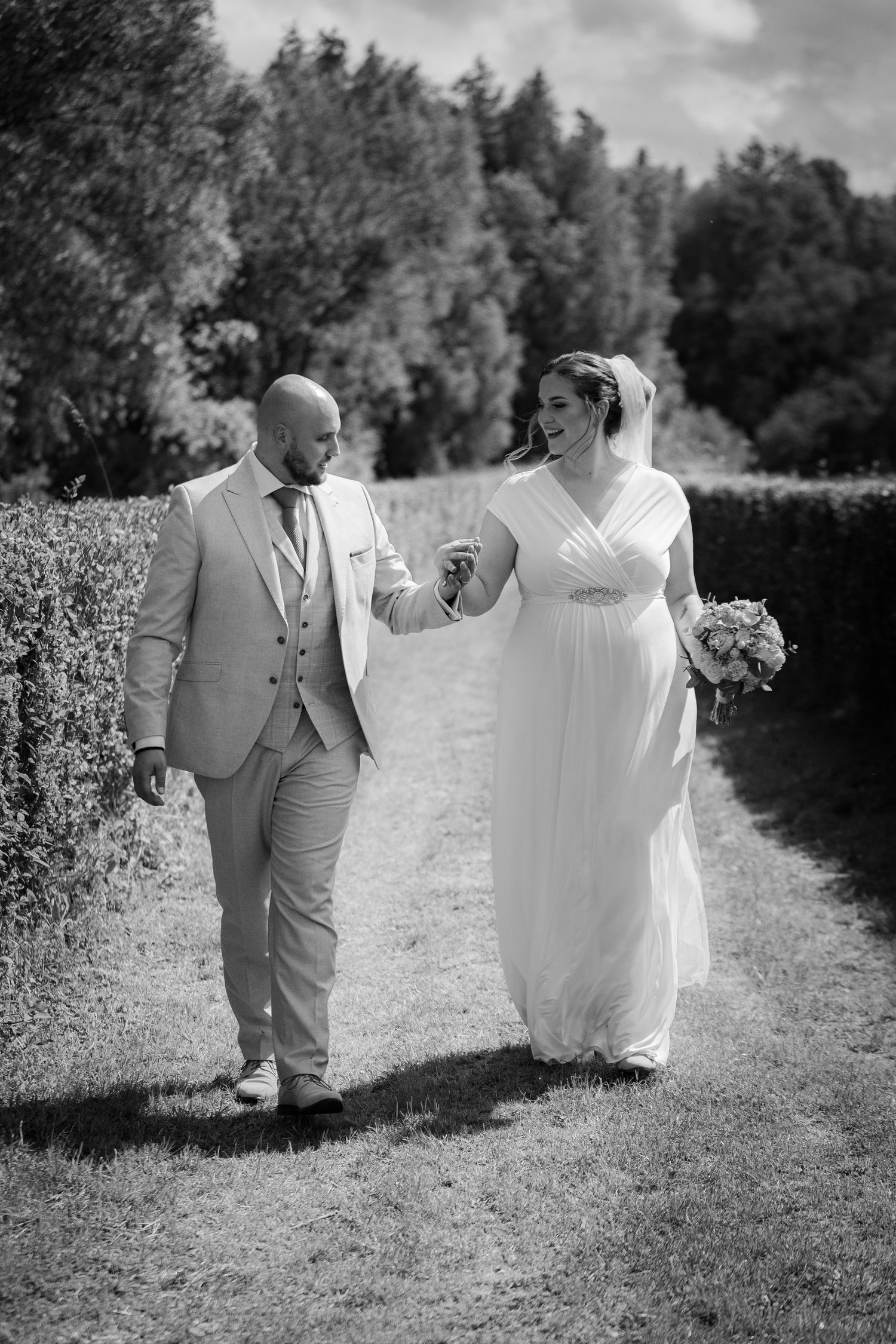 Black and white photo of couple walking and laughing together on garden path.