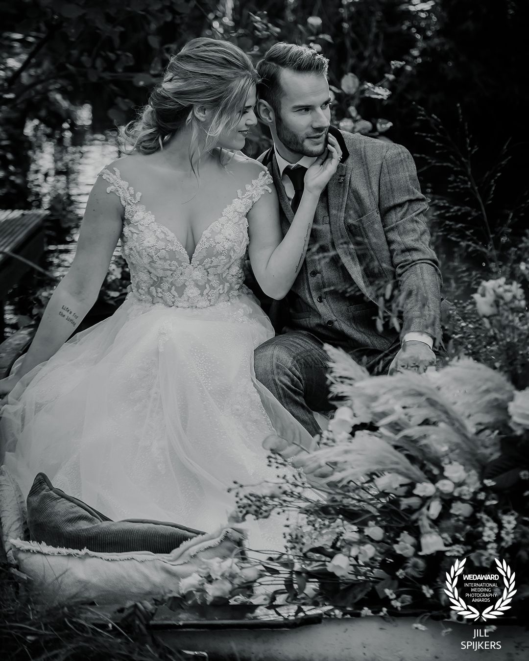 Intimate black and white portrait of couple in wedding attire sitting in garden setting.