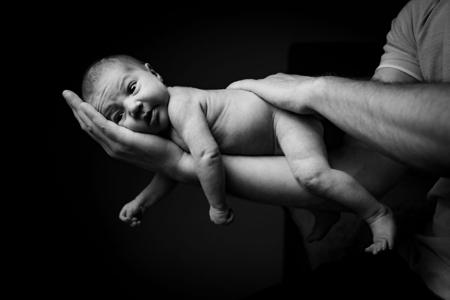 Artistic black and white photo of gentle hands holding a newborn baby.