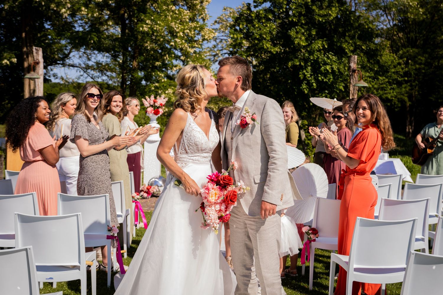 Wedding couple walking down the aisle while guests in coral and gray dresses look on.