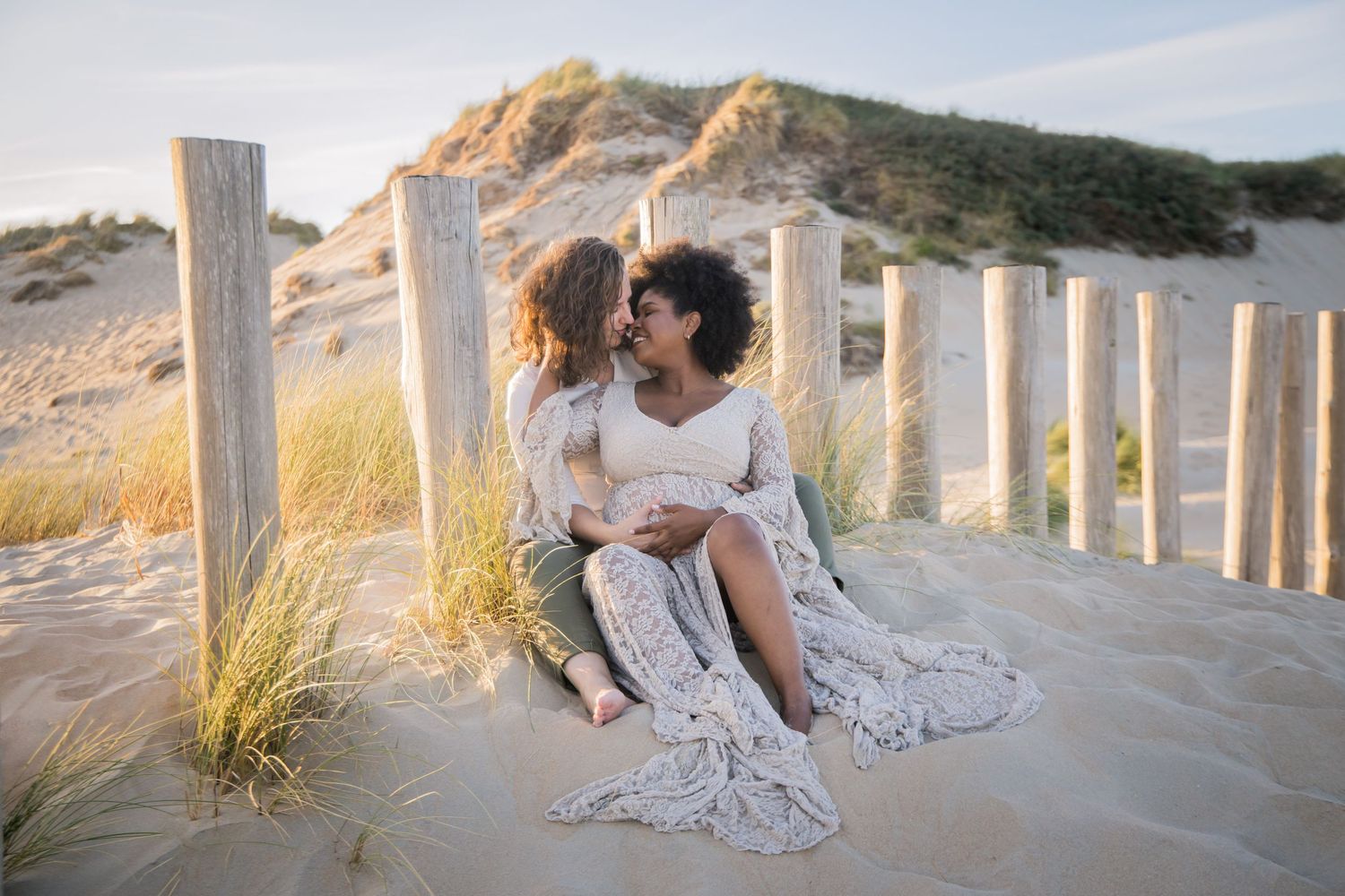 Romantic scene on sandy beach with white fence posts and flowing dress in evening light.