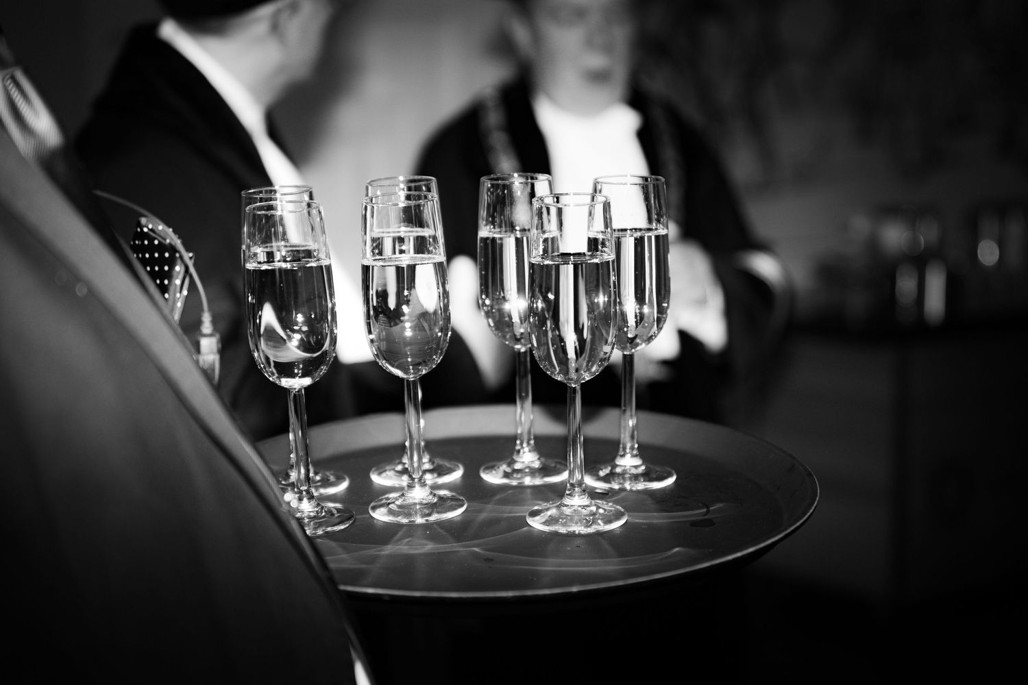 Black and white close-up of champagne glasses on server's tray.