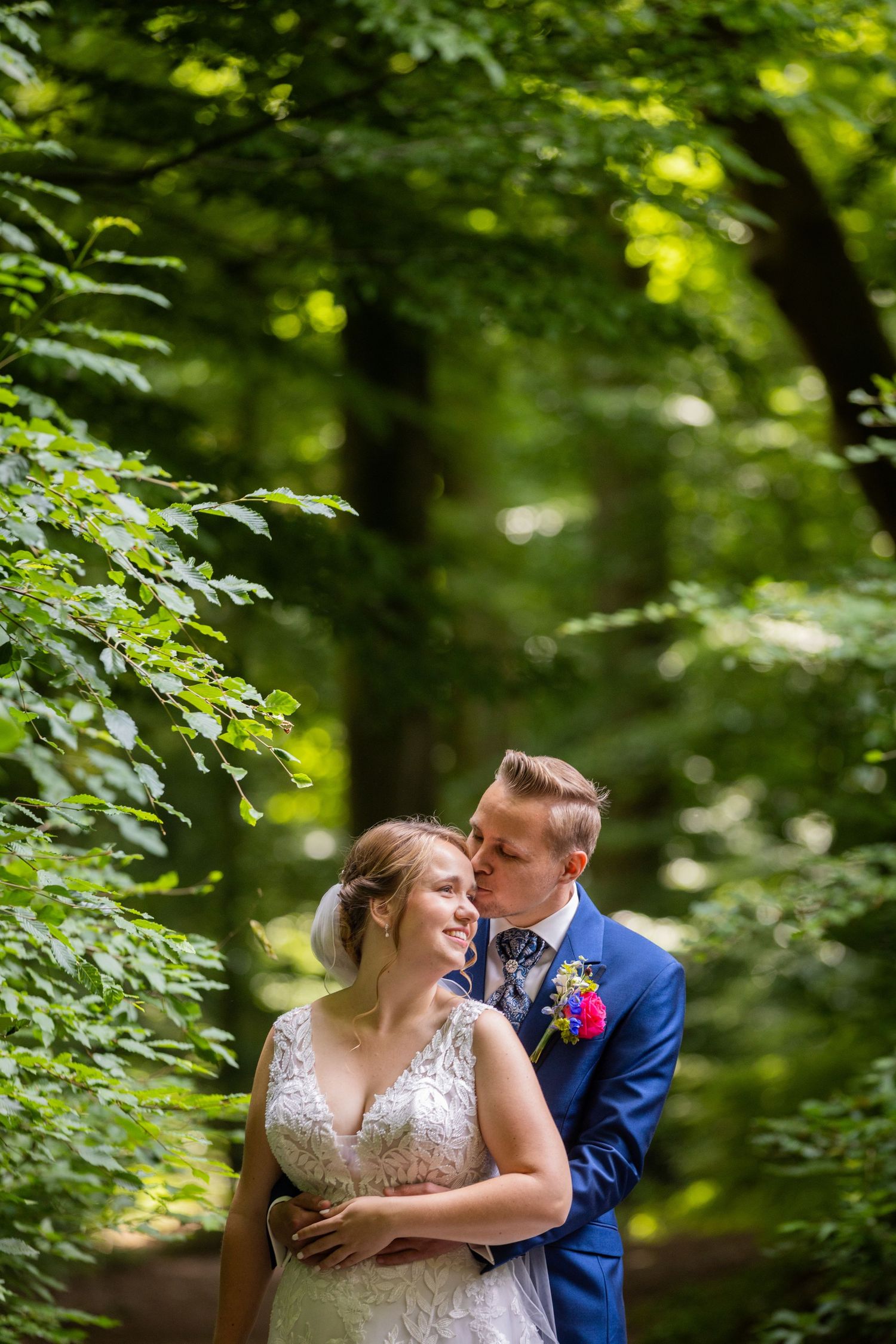 Intimate moment between couple in wooded setting with dappled sunlight filtering through trees.