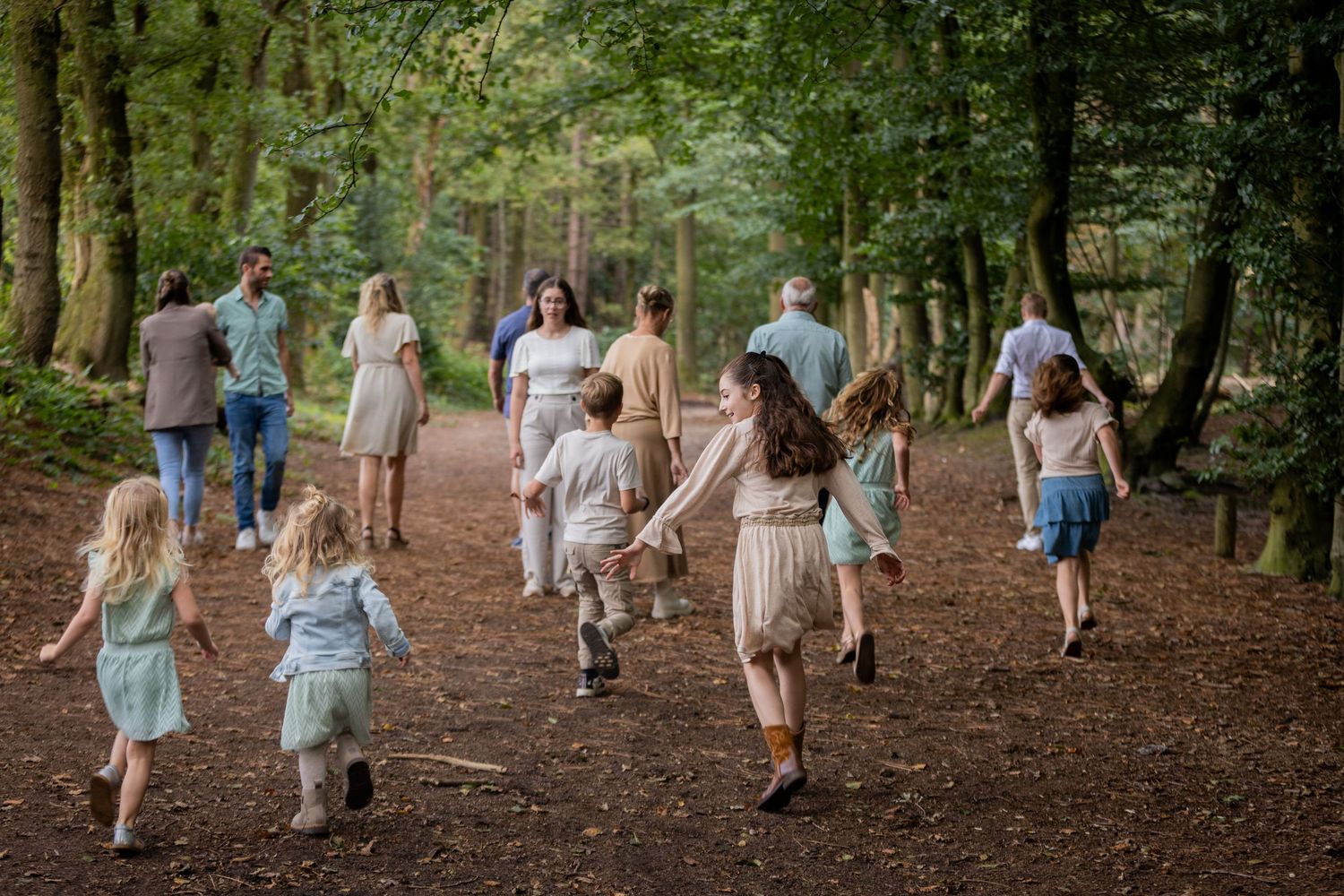 A joyful group runs together down a forest path wearing light summer clothing in natural lighting.