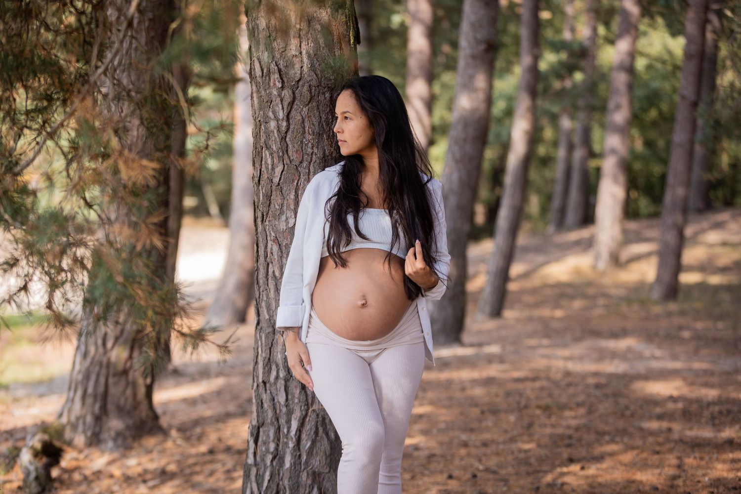Maternity portrait in forest setting with mother wearing light colored athletic wear.