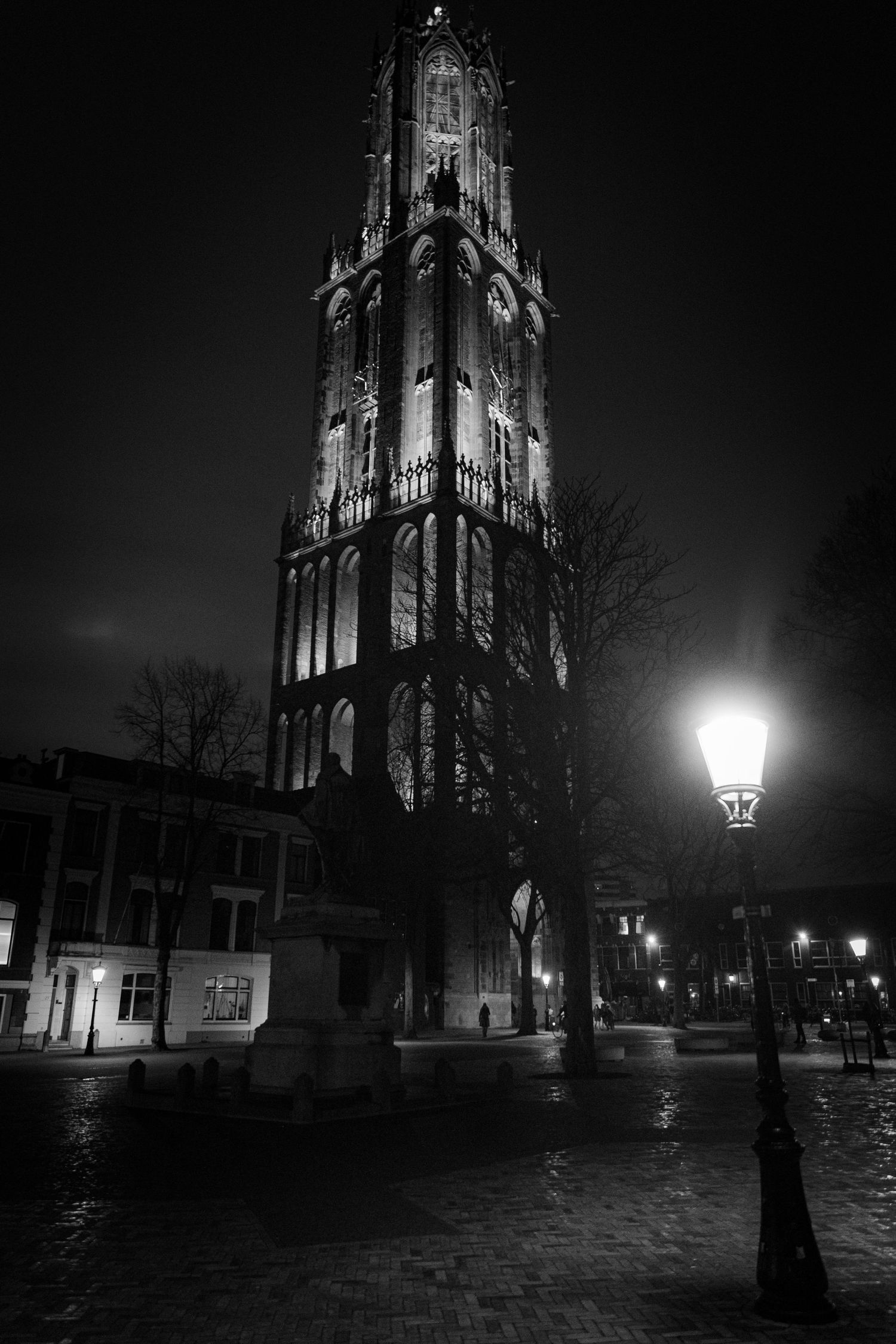 Dramatic black and white nighttime view of a Gothic cathedral tower illuminated against dark sky.