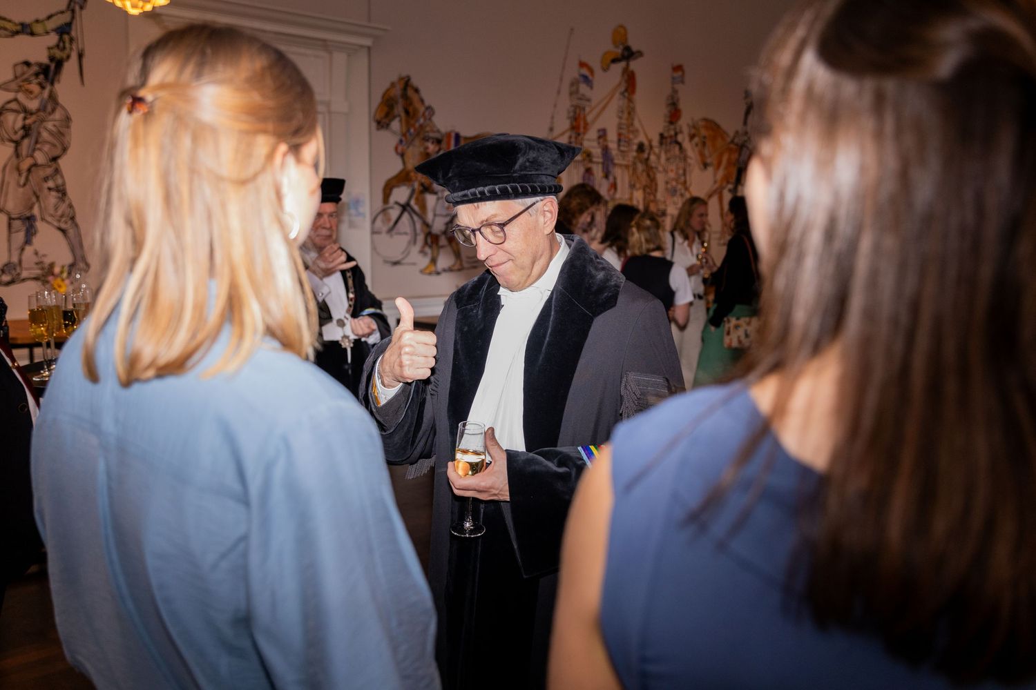 Academic figure in traditional cap and robe speaks with attendees at formal university event.
