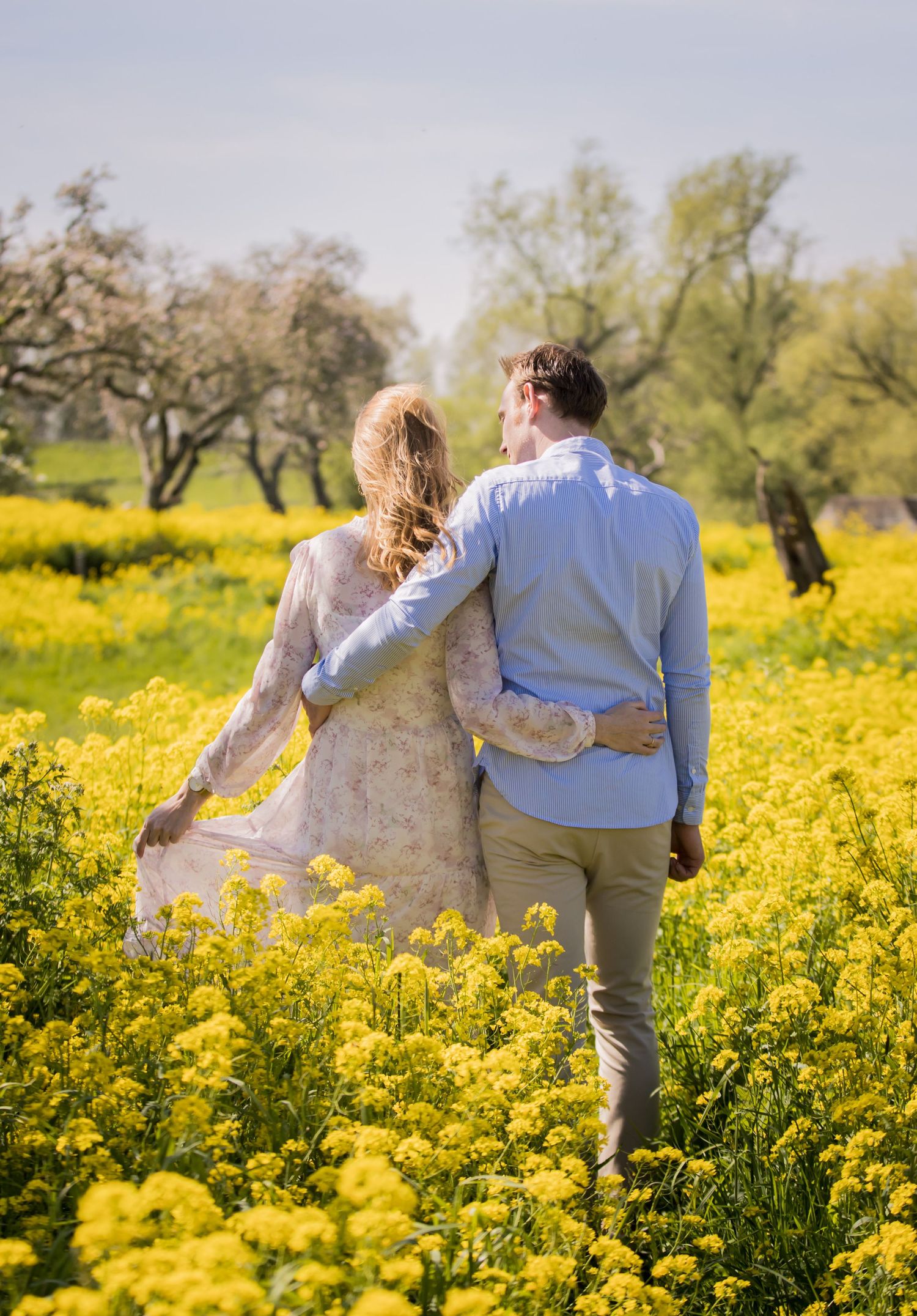 A couple walks hand in hand through a meadow of bright yellow wildflowers on a sunny afternoon.