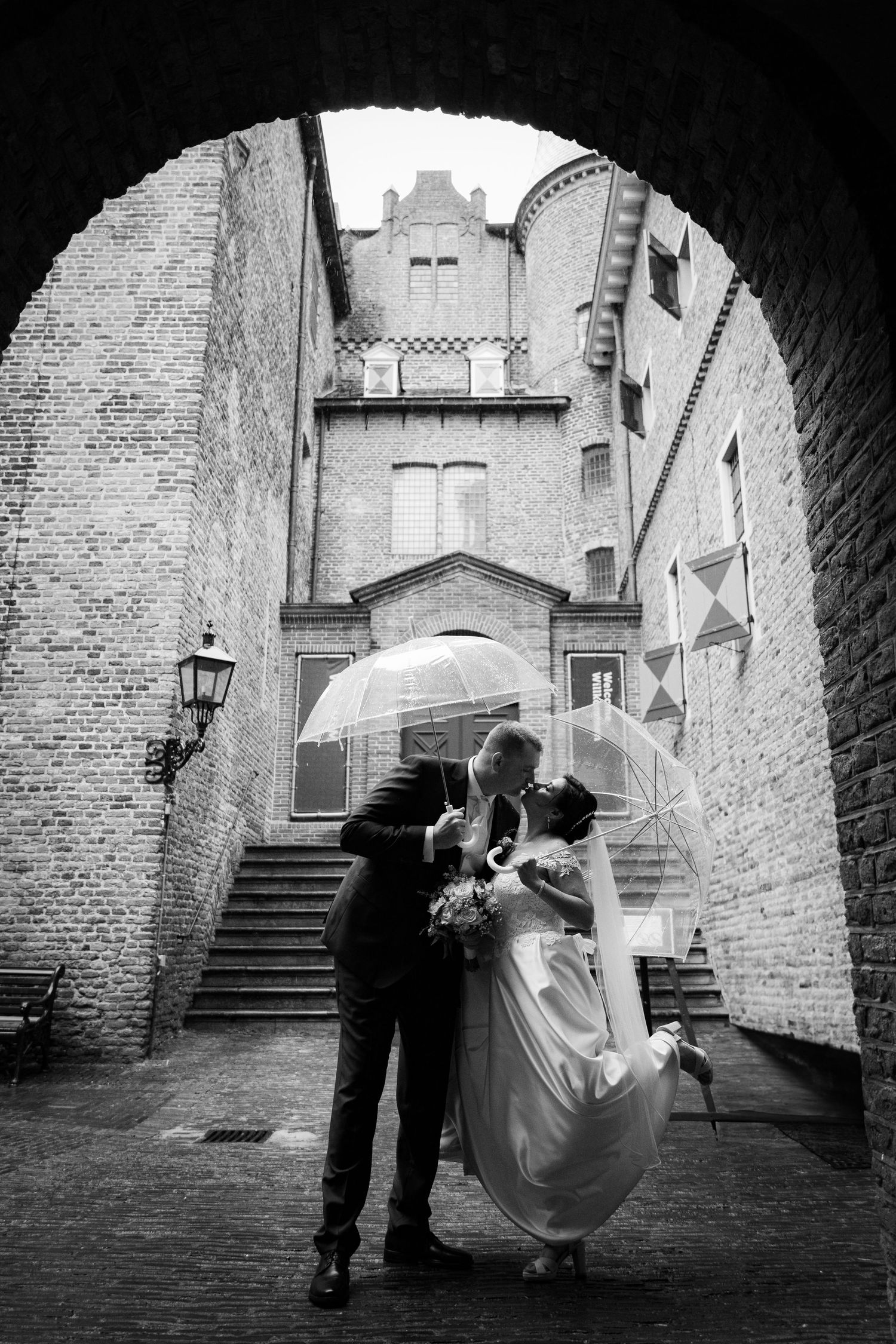 Black and white wedding photos capture couple walking through historic brick archways.