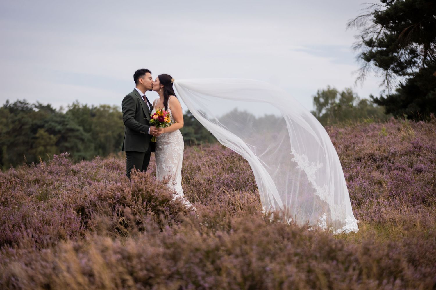 A dramatic wedding portrait with flowing veil against a mountain landscape.