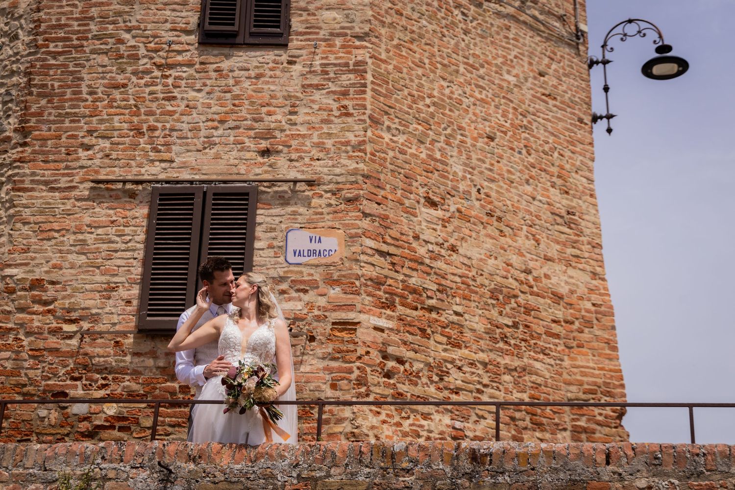 Two people embracing against rustic brick wall with vintage street lamp in Italian town of Montalcino.