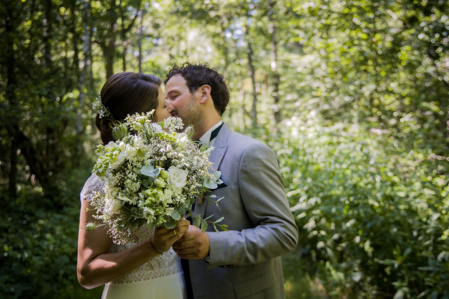 Intimate wedding portrait of couple embracing in sunlit forest setting.