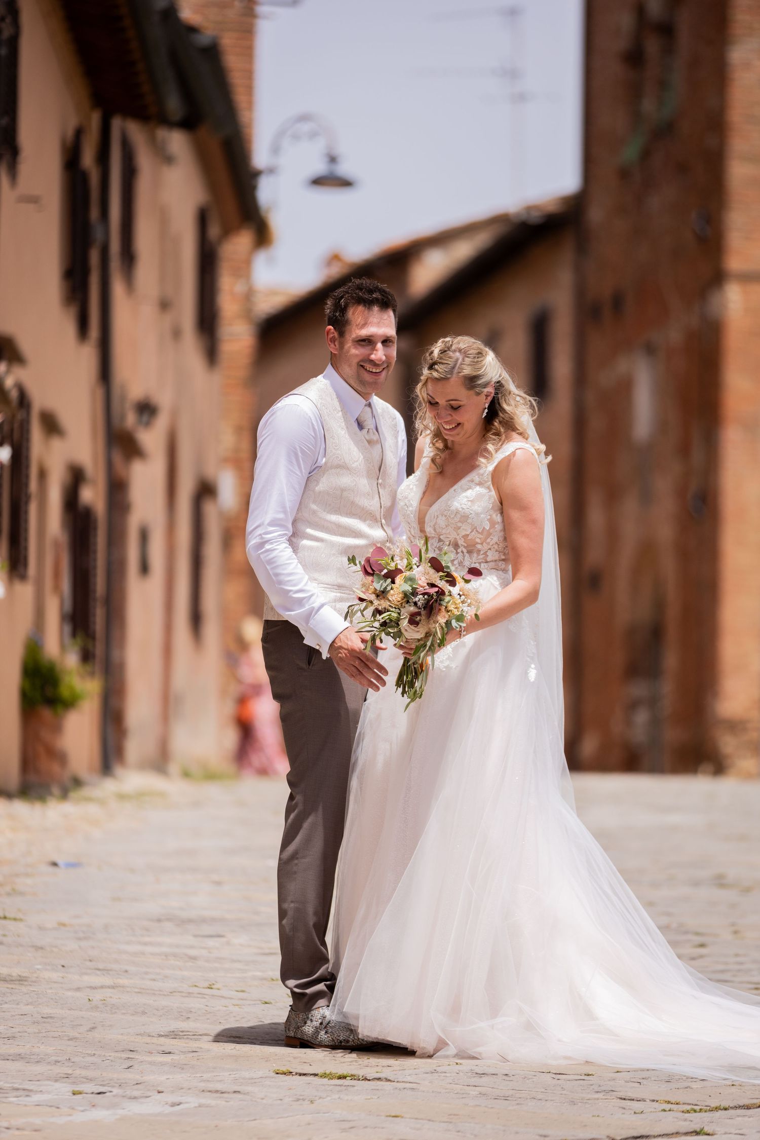Elegant couple posing in a rustic Italian village street with stone architecture and warm lighting.