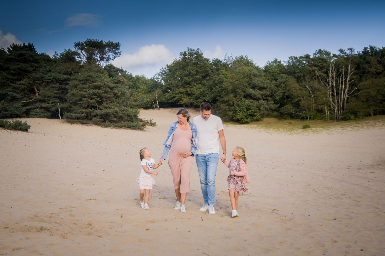 A family walks together on a sandy beach bordered by green trees on a sunny day.