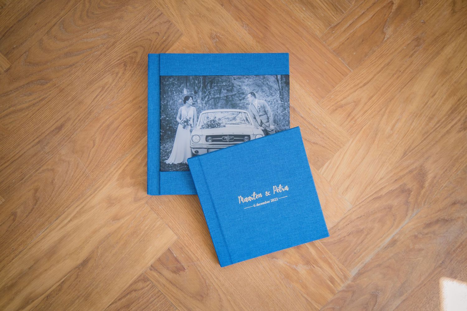 Two bright blue wedding photo album books lying on a wooden parquet floor.