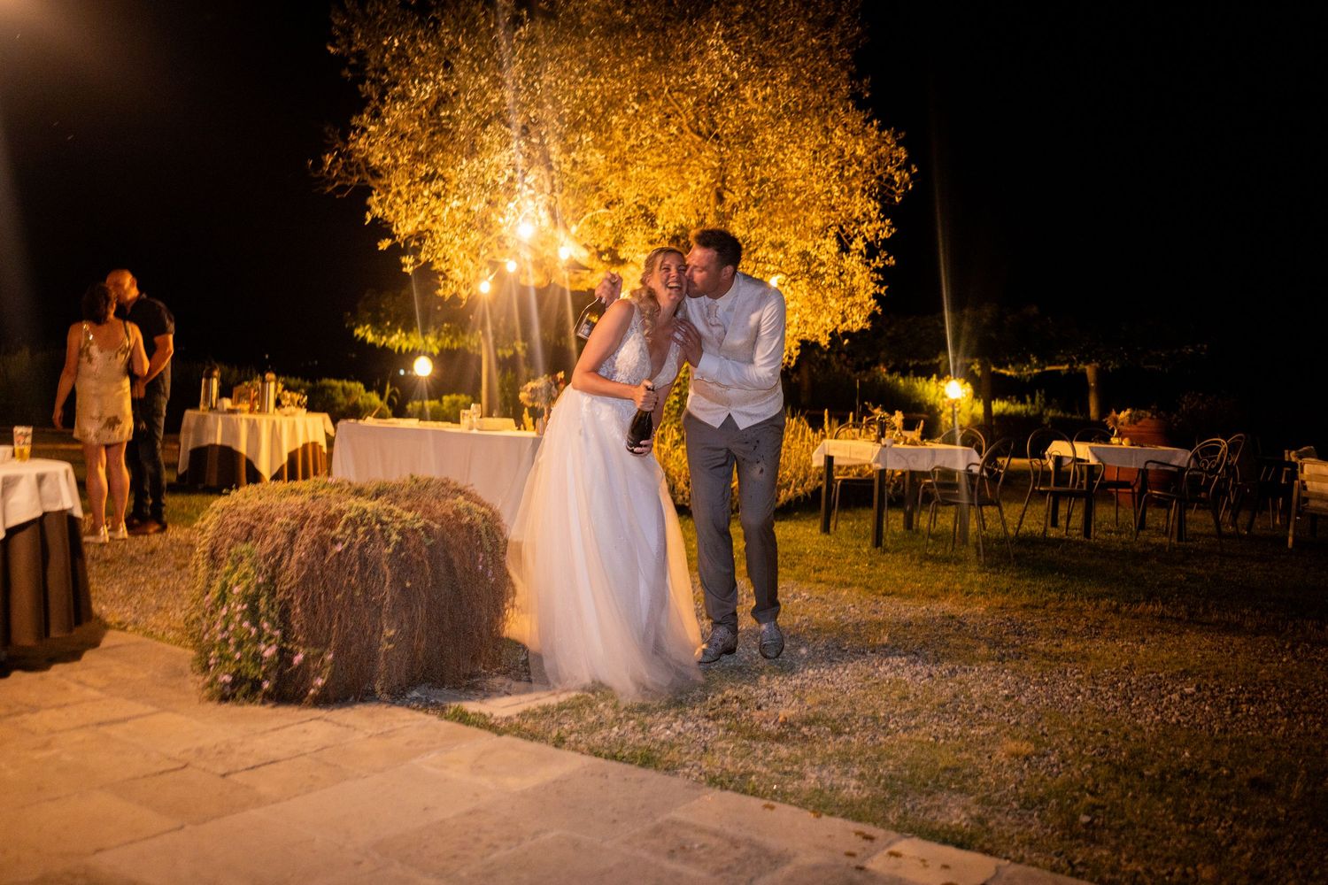 A bride and groom celebrate their romantic sparkler exit at a nighttime outdoor wedding ceremony under glowing trees.