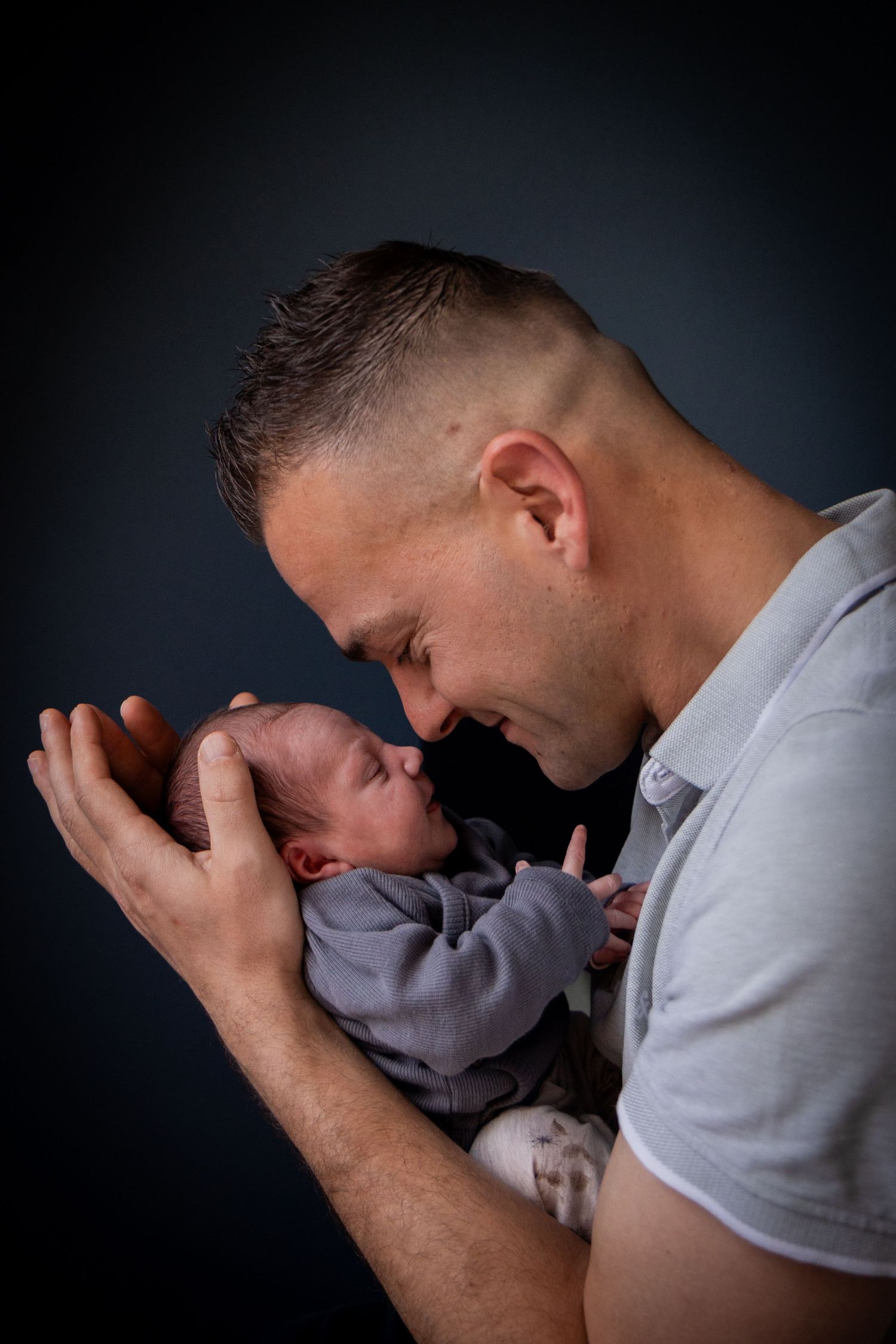 Intimate portrait of a parent cradling newborn baby against dark background.