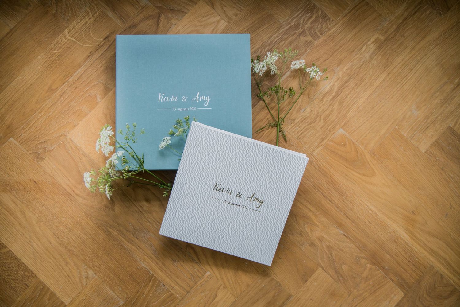 Two wedding photo albums in light blue and white with delicate baby's breath flowers on wooden floor.