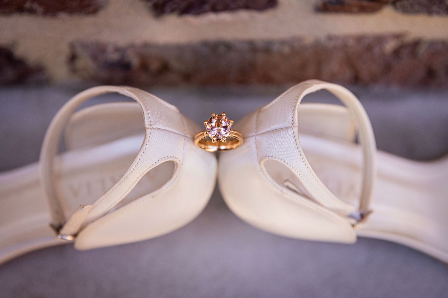 Wedding ring placed artistically between white bridal shoes.
