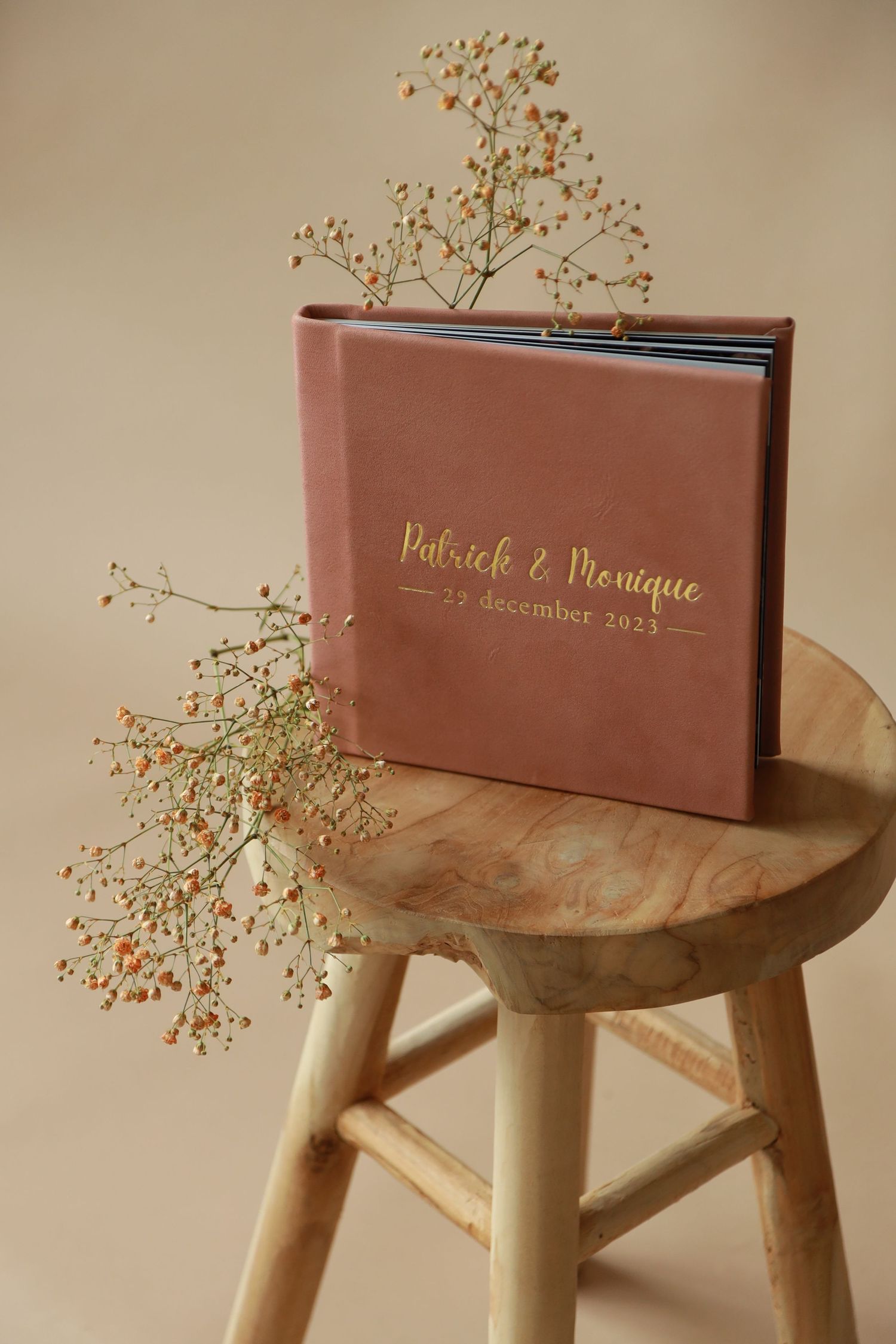 Dusty rose photo album with gold lettering on wooden stool decorated with delicate baby's breath flowers.